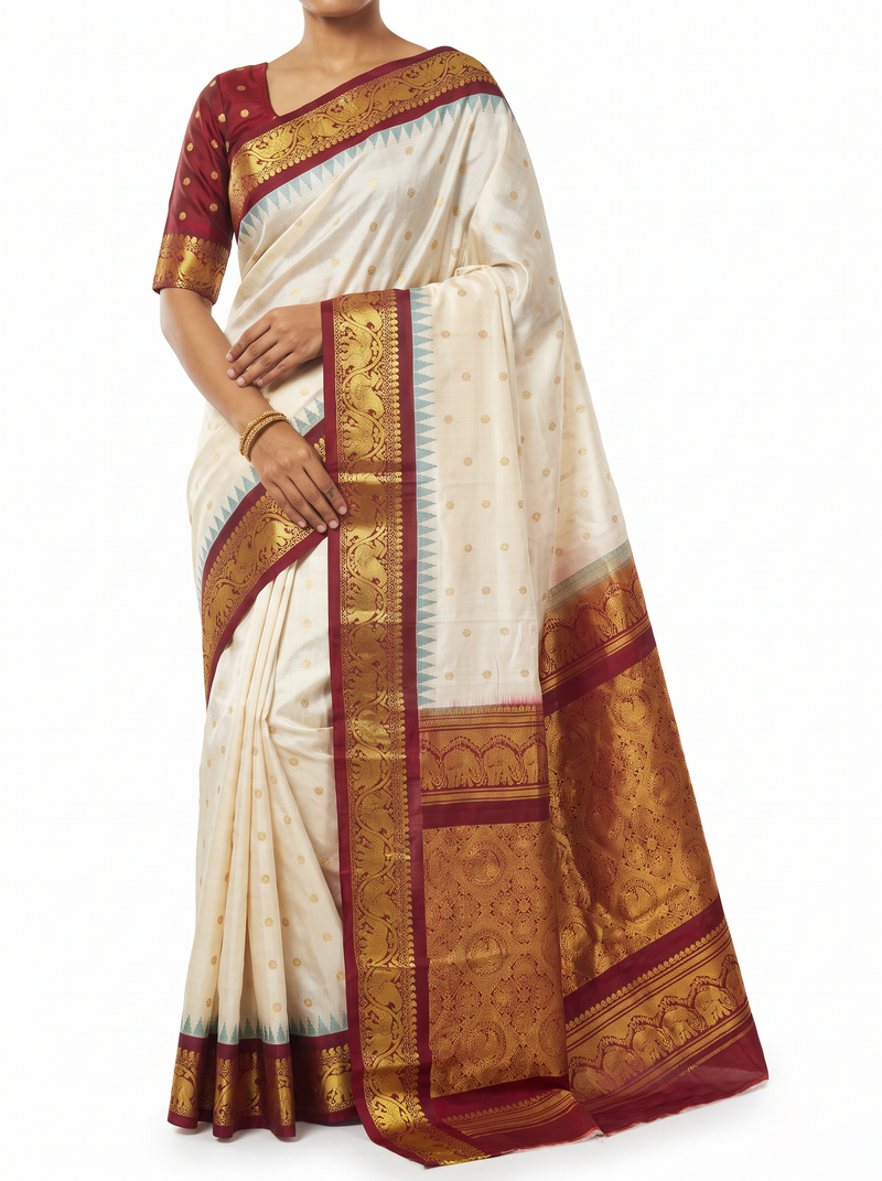 Soft cream scattered with gold, meeting rich maroon where zari elephants march through a golden jaal. Handloom Gadwal silk.