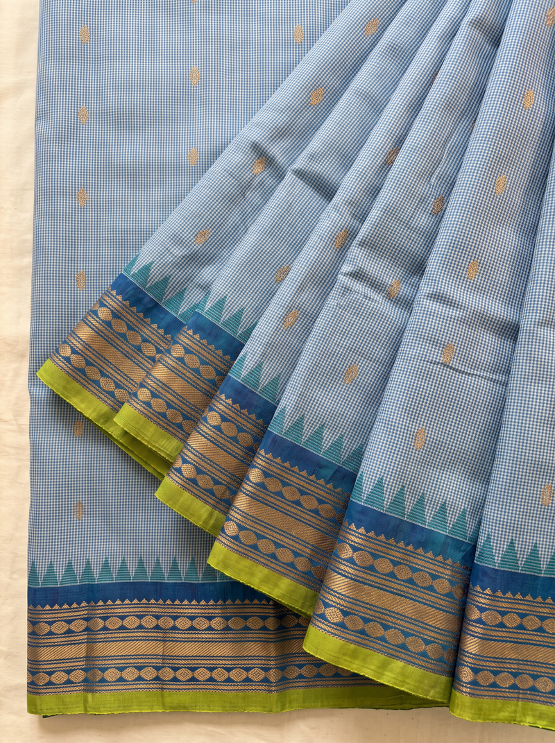 Soft as a morning sky, powder blue silk scattered with gold, deepening into royal blue where zari peacocks rest in a golden jaal. Handloom Gadwal.