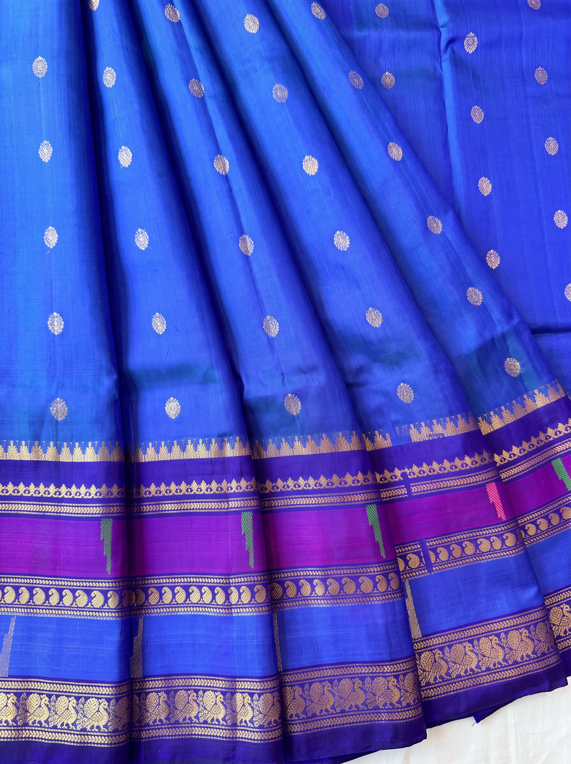 Like a clear midnight sky sprinkled with golden stars, this blue Gadwal silk is edged with peacocks and a blush of pink, finishing in a pallu rich with gold zari.