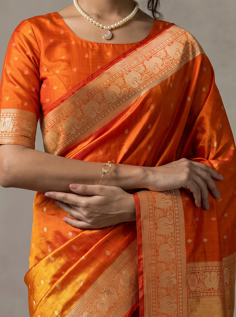 Like firelight caught in silk, orange-gold tissue glints with silver butas, while red peacocks guard the border and the golden pallu glows with lattice and a red fringe. Handloom Gadwal.