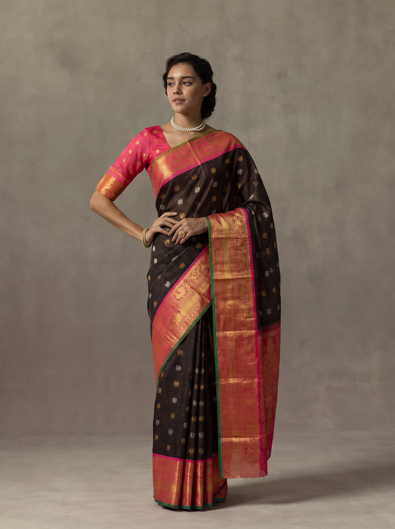 Gadwal - Handloom Gadwal silk in deep black zari checks with gold and silver butas. Its peach gold border and pallu glow with maroon pink paisleys and florals.