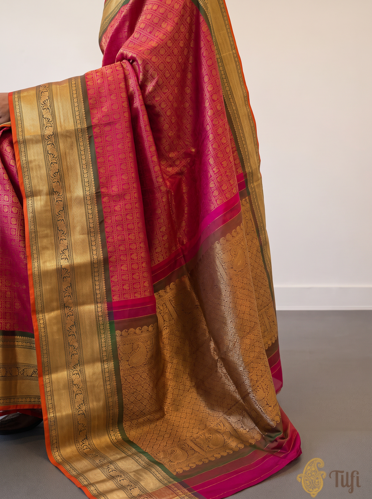 Like a lotus resting on dark leaves, vibrant pink silk glints with gold checks and opens into deep green, where brocade flowers glow in gold. Handloom Gadwal.