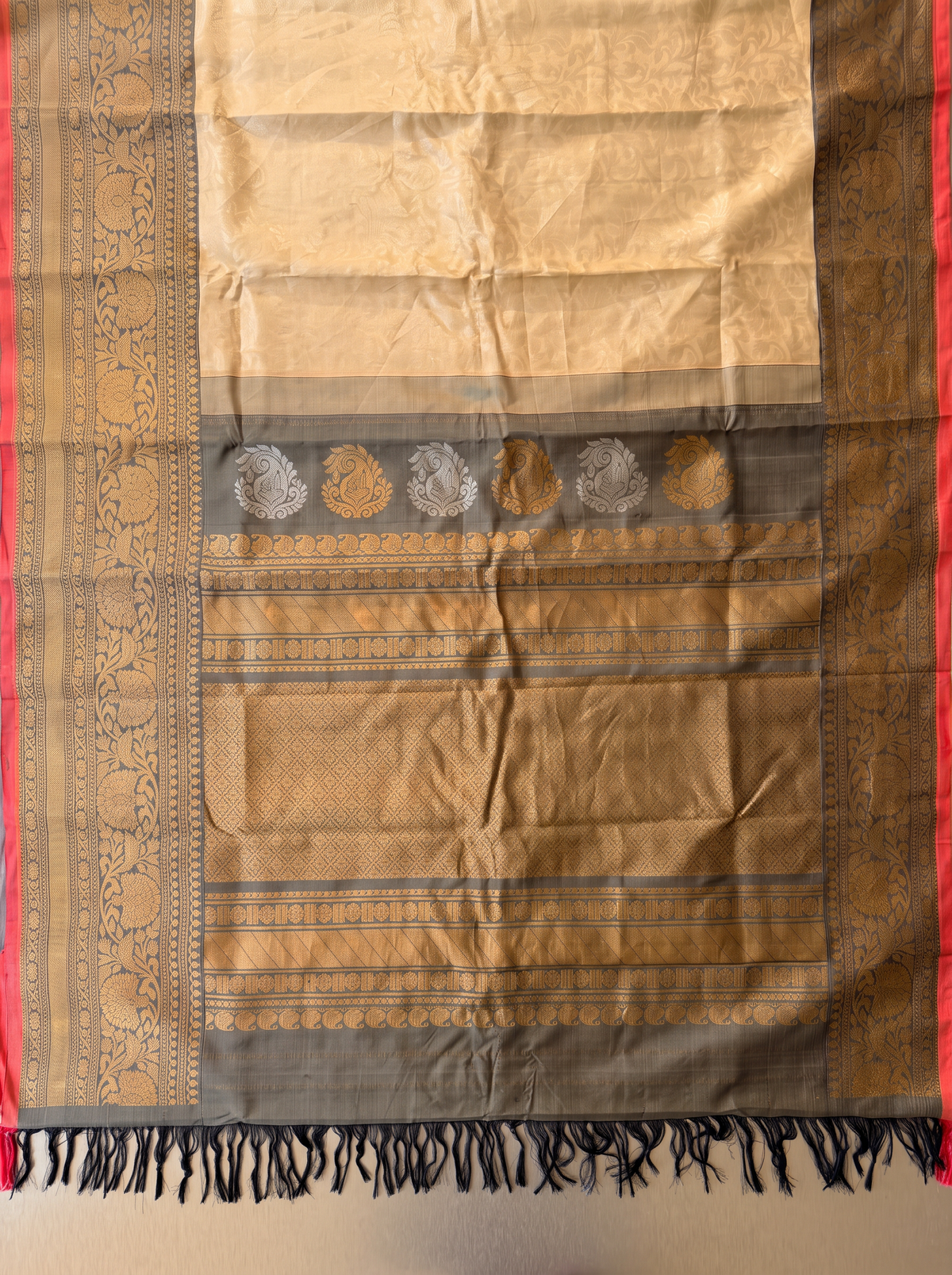 Like morning light on stone, soft cream meets warm grey, lit by a coral red edge and a shimmering gold zari jaal. Handloom Gadwal silk.