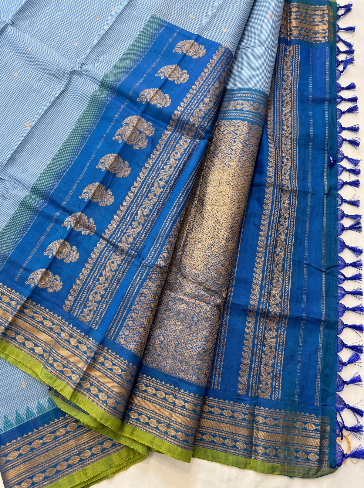 Soft as a morning sky, powder blue silk scattered with gold, deepening into royal blue where zari peacocks rest in a golden jaal. Handloom Gadwal.