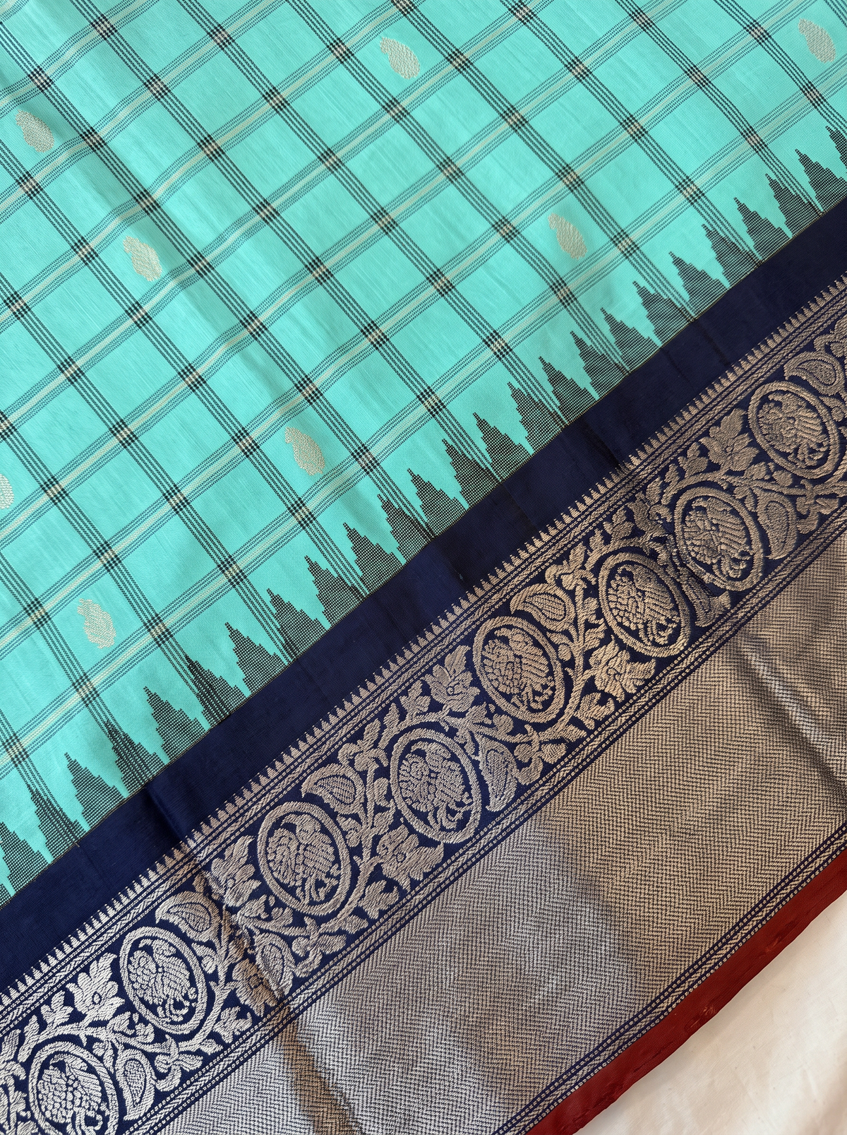 Like a lotus pond under moonlight, sea green silk shimmers with silver butas and fine checks, meeting navy depths and a silver tissue pallu full of zari blossoms. Handloom Gadwal.