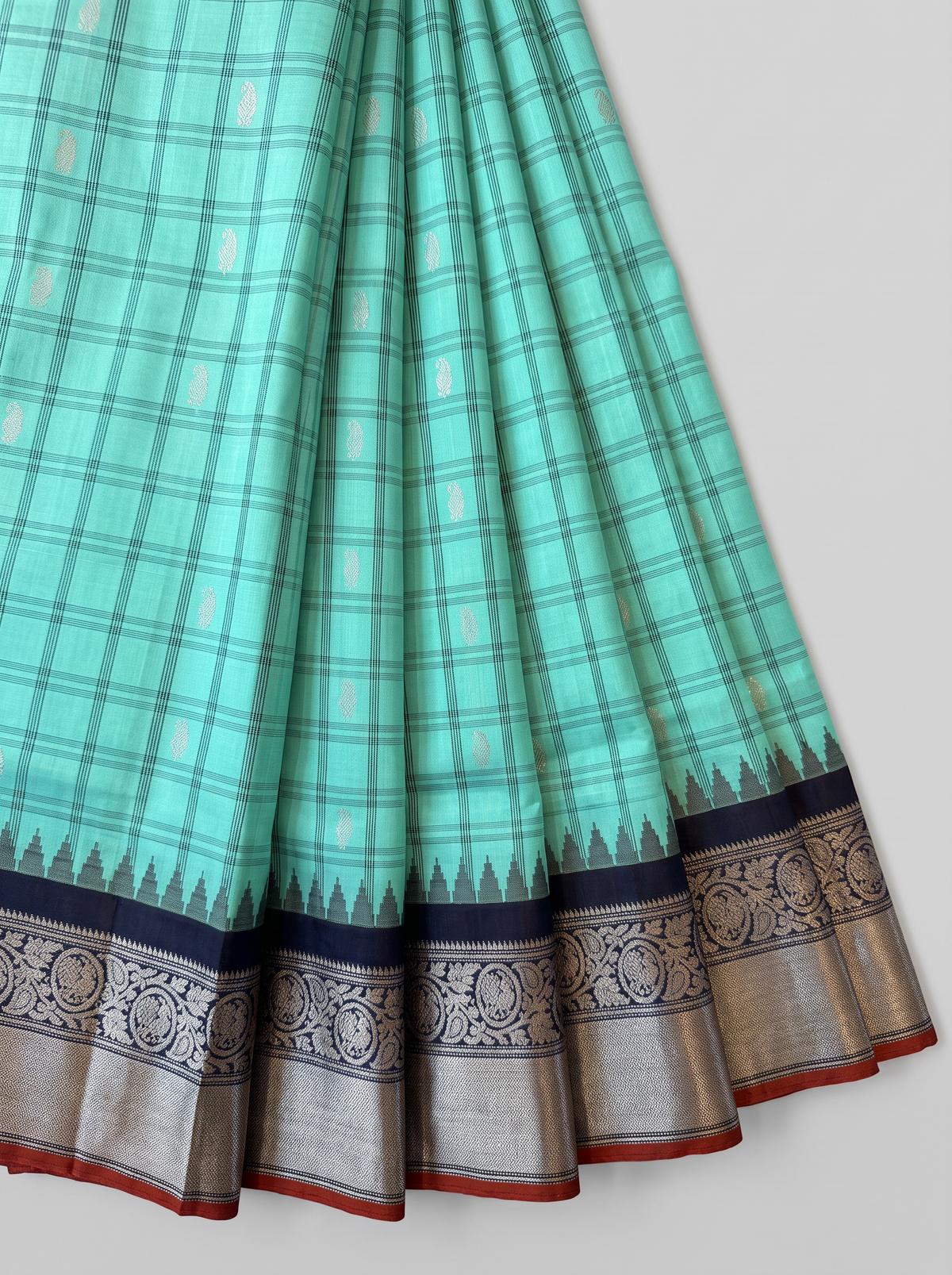 Like a lotus pond under moonlight, sea green silk shimmers with silver butas and fine checks, meeting navy depths and a silver tissue pallu full of zari blossoms. Handloom Gadwal.