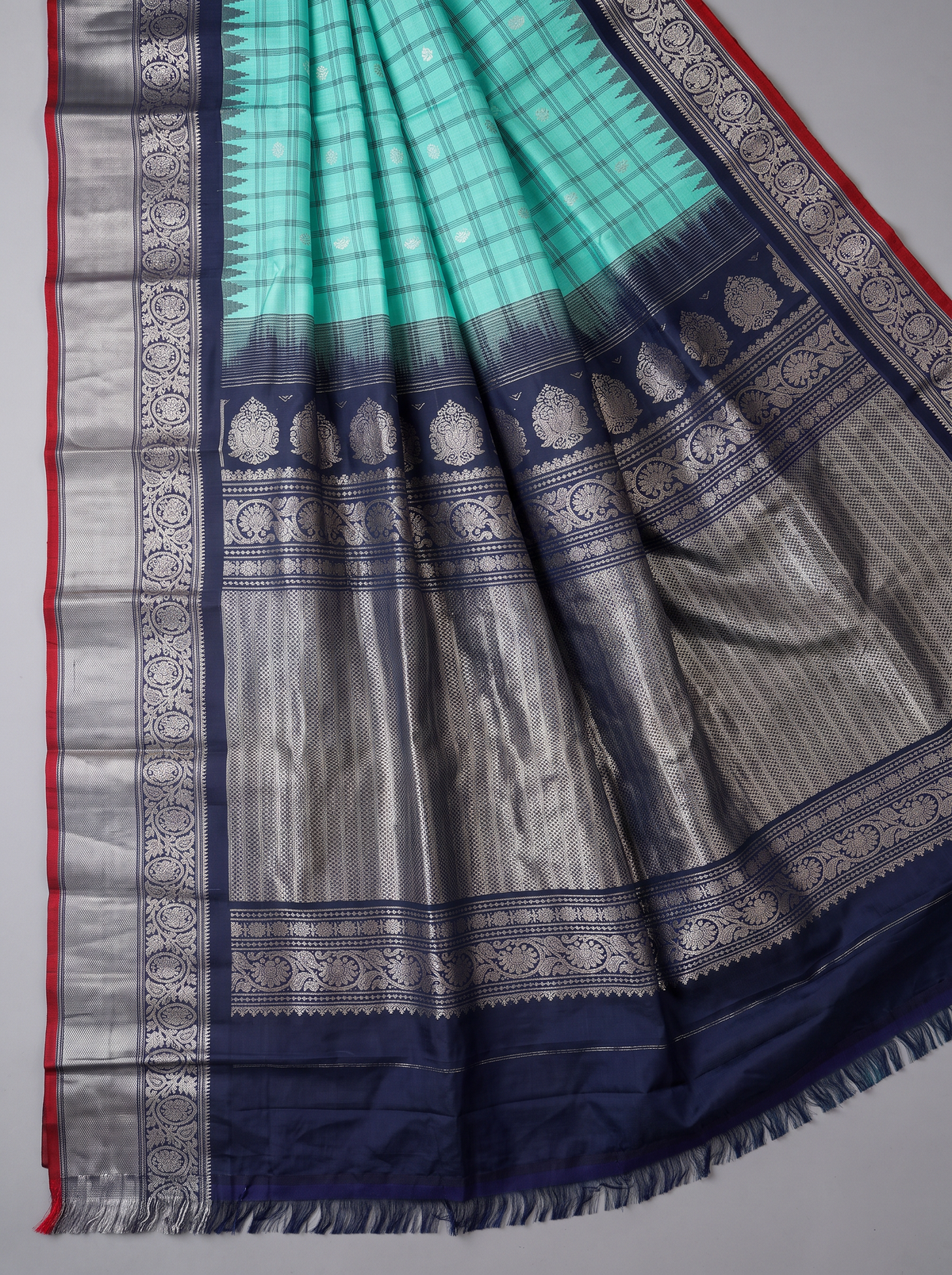 Like a lotus pond under moonlight, sea green silk shimmers with silver butas and fine checks, meeting navy depths and a silver tissue pallu full of zari blossoms. Handloom Gadwal.
