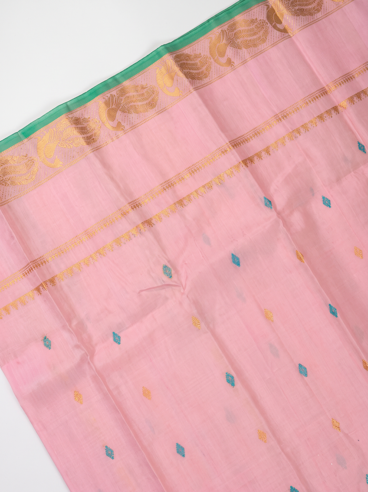 A blush of pink, a sprinkle of gold and teal, and peacocks in shimmering zari dancing along a green edge. Pure silk Gadwal, handwoven with love in Telangana.