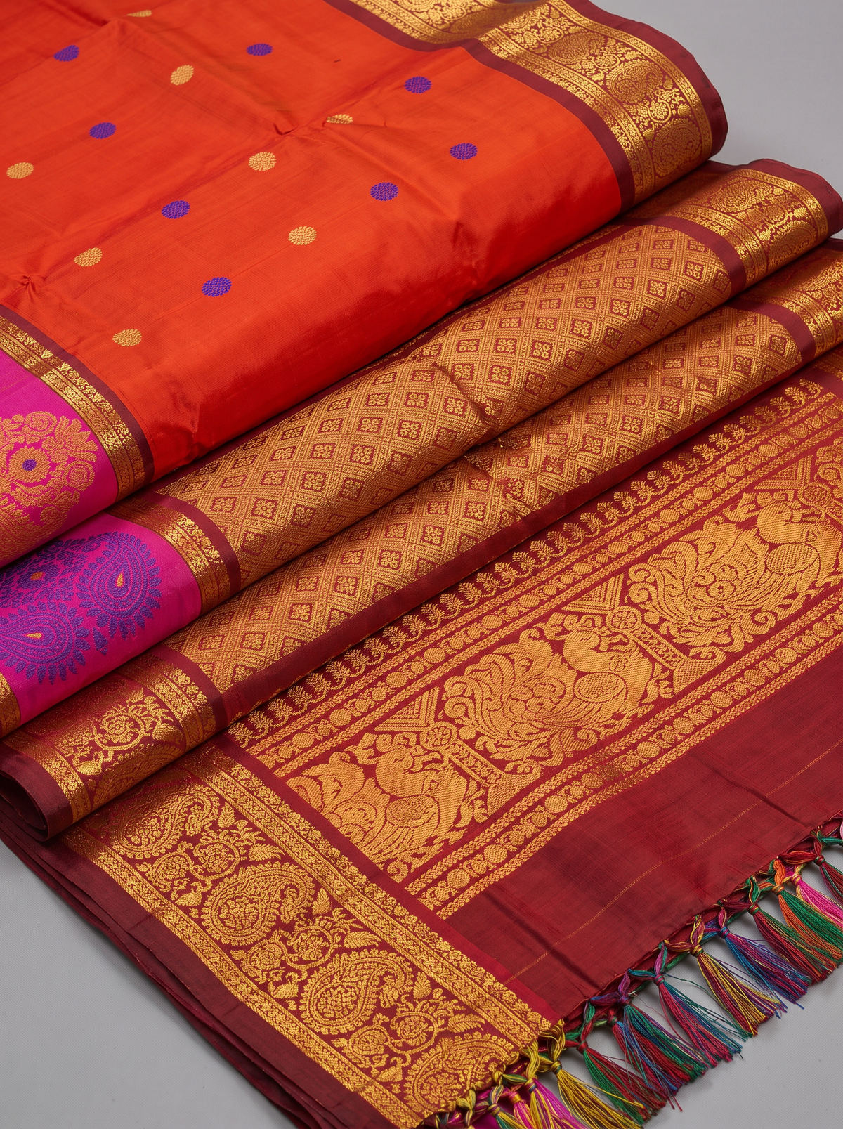 Like a marigold in full bloom, this orange Gadwal silk glows with gold and blue butis. A pink-edged maroon border holds it close, and the pallu shines in rich gold zari.