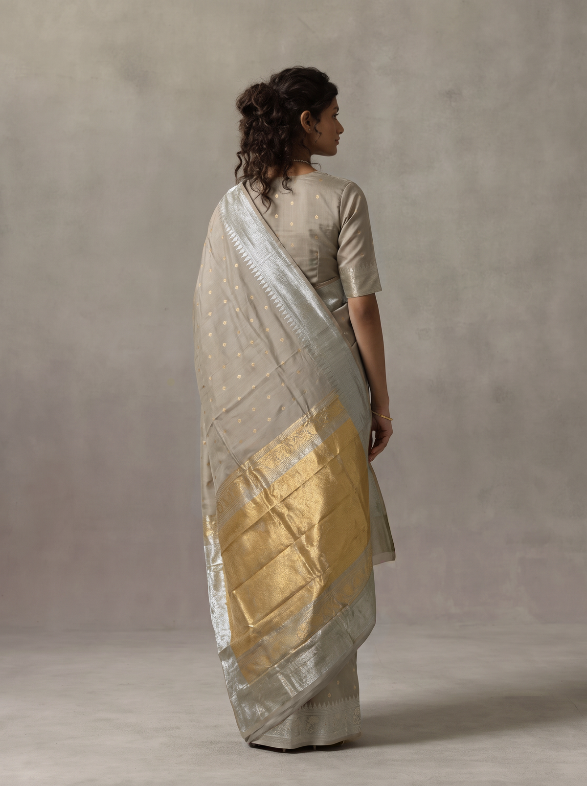 Soft as a winter morning, dove grey silk glints with tiny gold butas, and its tissue pallu glows like moonlight and sunlight woven together. Handloom Gadwal.