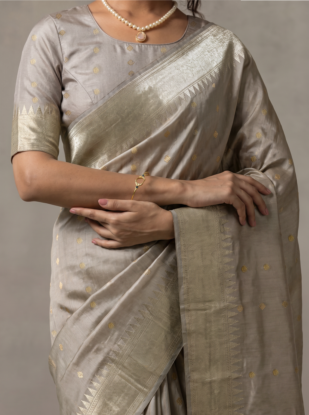 Soft as a winter morning, dove grey silk glints with tiny gold butas, and its tissue pallu glows like moonlight and sunlight woven together. Handloom Gadwal.