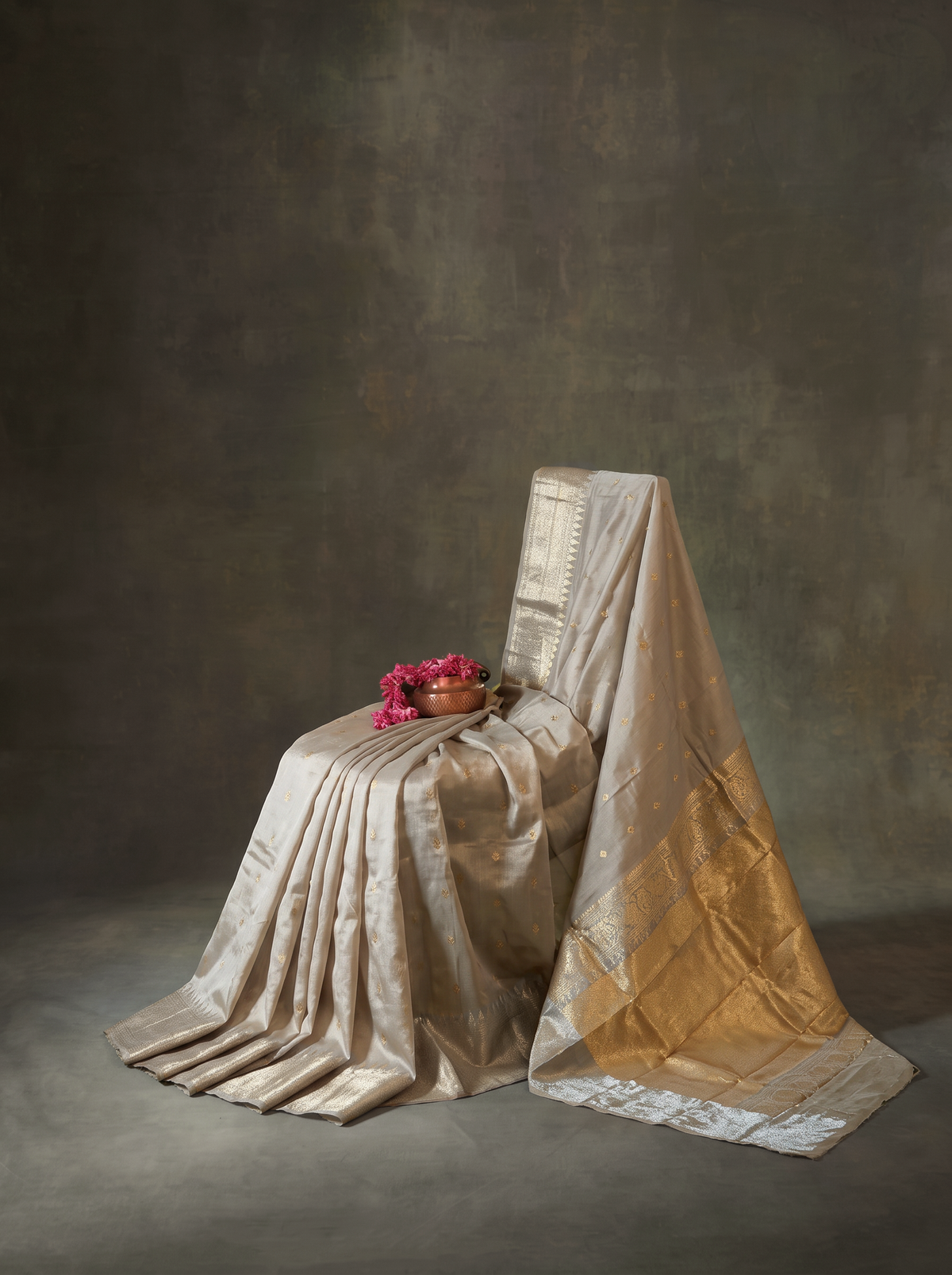 Soft as a winter morning, dove grey silk glints with tiny gold butas, and its tissue pallu glows like moonlight and sunlight woven together. Handloom Gadwal.