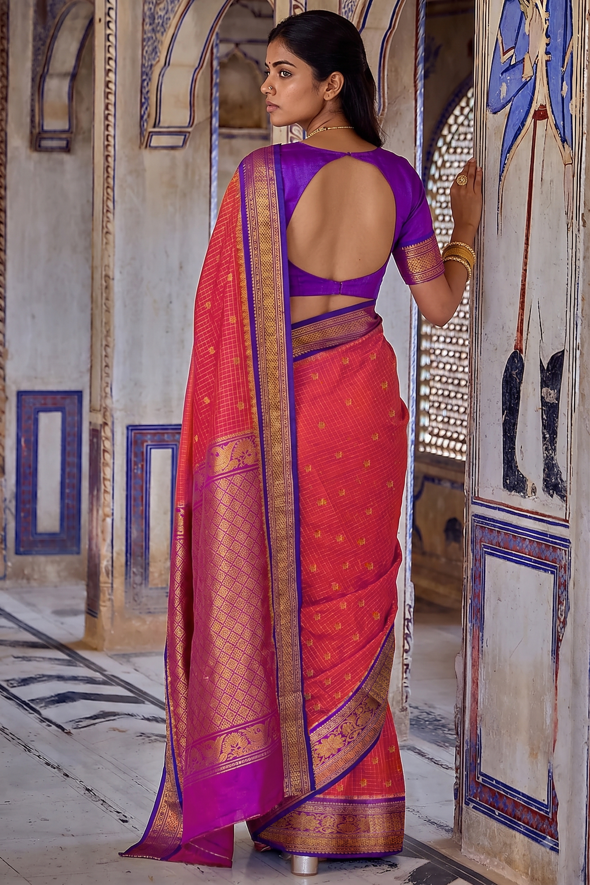 A burst of rani pink, patterned with gold checks and tiny buttis like confetti, held close by deep purple, where a golden jaal shimmers across the border and pallu.